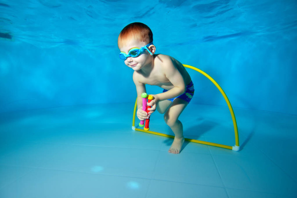 Roztomilá mimino ponory pod vodou a vytahuje hračky ze dna bazénu. Portrét. Podvodní fotografie. Vodorovná orientace - Fotografie, Obrázek