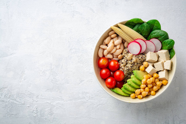Healthy vegan buddha bowl with spinach, tomato, chickpea, quinoa, radish, beans, avocado, mini corn and tofu cheese on concrete background. Top view. Copy space. - Фото, изображение
