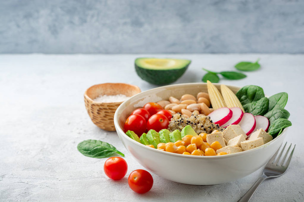 Healthy vegan buddha bowl with spinach, tomato, chickpea, quinoa, radish, beans, avocado, mini corn and tofu cheese on concrete background. Selective focus. - Zdjęcie, obraz