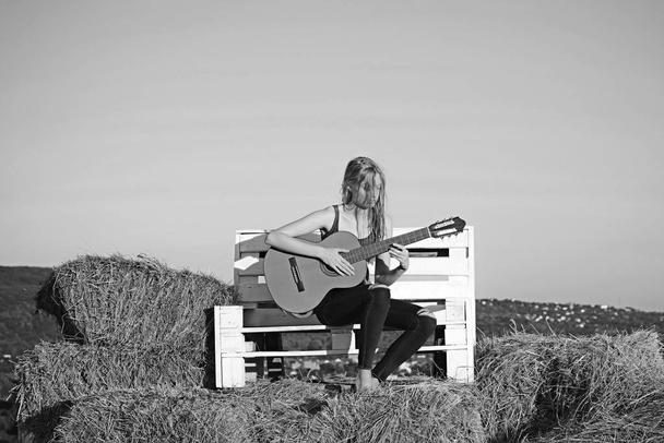 Fashion woman play guitar on wooden bench. Fashion musician with string instrument on sunny nature - Fotografie, Obrázek