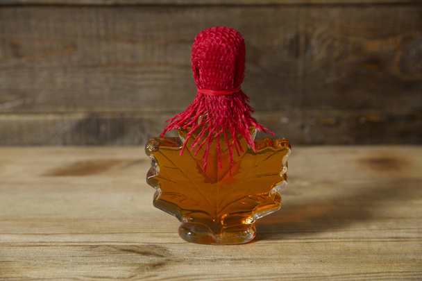  maple syrup in a glass bottle in the form of a maple leaf on a wooden rustic background with copy space for text - Foto, afbeelding