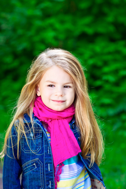 Outdoor portrait of an adorable smiling blond little girl wearing a jeans jacket a pink scarf - Photo, Image