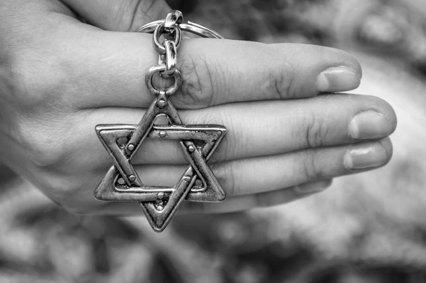 Ręka młodej kobiety posiadając kluczowy łańcuch z gwiazdą Dawida, tradycyjnym symbolem żydowskim. Obraz koncepcyjny międzynarodowego dnia pamięci o Holokauście, pomnik Holokaustu. Czarno-biały obraz. - Zdjęcie, obraz