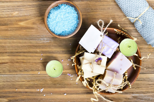 Přírodní mořská sůl v nádobě a domácí mýdlo prezentované na hnědém dřevěném stole s prostorem pro kopírování. Plochá ležela - Fotografie, Obrázek