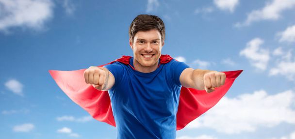 man in red superhero cape over sky background - Foto, afbeelding