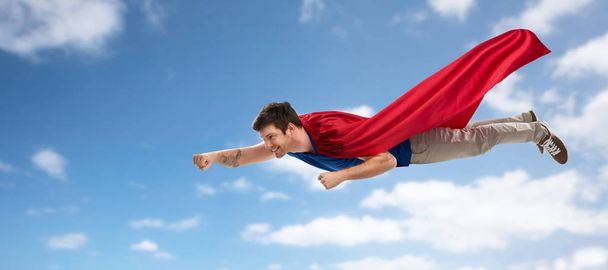 man in red superhero cape flying over sky - Фото, изображение