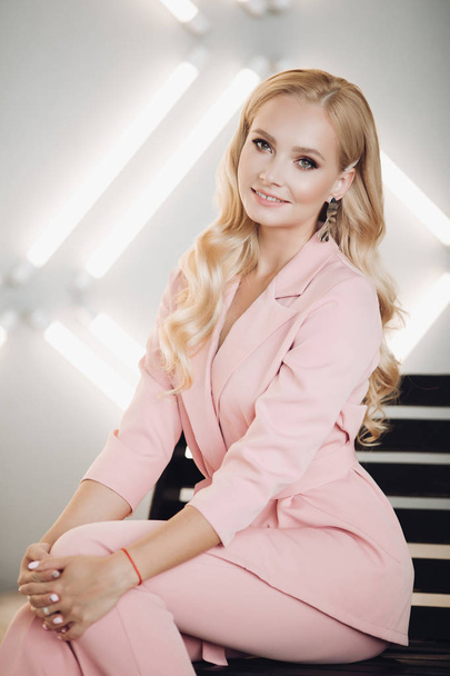 Ξανθιά σε ροζ έξυπνο κοστούμι κάθεται στις σκάλες και ποζάρει - Φωτογραφία, εικόνα
