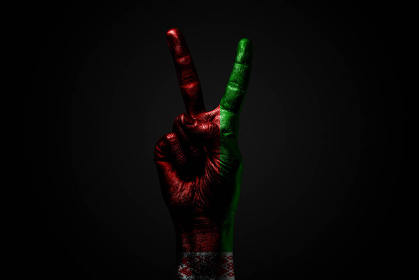 Une main avec un drapeau de Biélorussie dessiné montre un signe de paix, un symbole de paix, d'amitié, de salutations et de paix sur un fond sombre
. - Photo, image