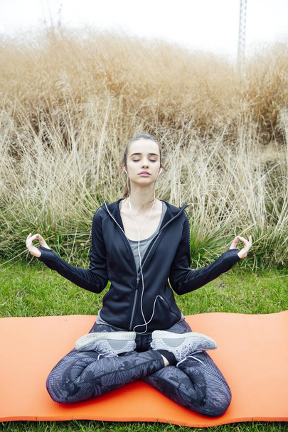junge Frau hört Musik und macht Yoga-Zen-Pose im Gras - Foto, Bild