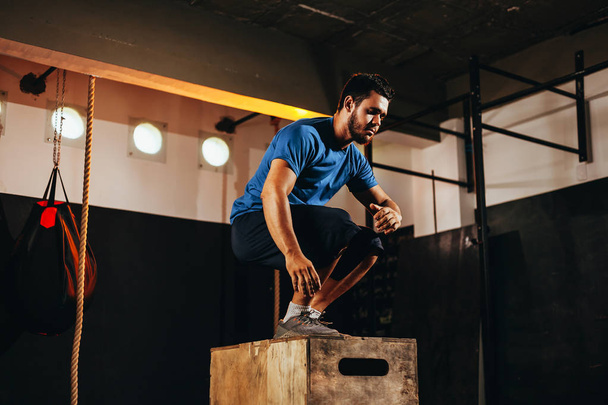 Fit young man doing a box jump exercise. Sports man doing a box squat at the gym - Foto, Imagem