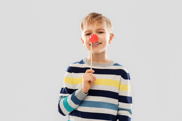 smiling boy with red clown nose party prop - 写真・画像