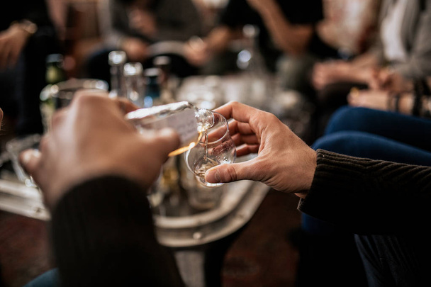 Ένα κοντινό πλάνο ενός άντρα που ρίχνει ουίσκι από ένα μπουκάλι. Έννοια του προστίμου αλκοόλ, γευσιγνωσία Γιαπωνέζικου ουίσκι. Μάστερ και γευσιγνωσία. - Φωτογραφία, εικόνα