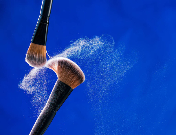 Make up brush with  powder explosion on blue background - Фото, зображення