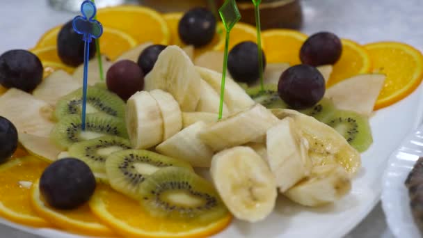 banai, πορτοκάλια, σταφύλια, ακτινίδιο κομμένα, κοντινό. νόστιμο φαγητό στο τραπέζι. Φρέσκα φρούτα σε ένα εορταστικό τραπέζι φαγητού. Ανάμεικτα ξυλάκια φρούτων σε φέτες σε ένα πιάτο. - Πλάνα, βίντεο