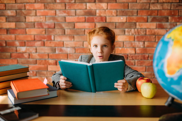 Aranyos iskoláslány a tankönyvek jelent az asztalnál. Női tanuló olvas egy könyvet az íróasztalon, fiatal lány csinál házi feladatot - Fotó, kép