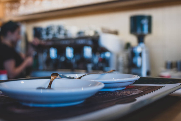 Άδειοι δίσκοι με κουτάλια στο προσκήνιο ενός καφέ με μηχανή καφέ bokeh στο παρασκήνιο.  - Φωτογραφία, εικόνα