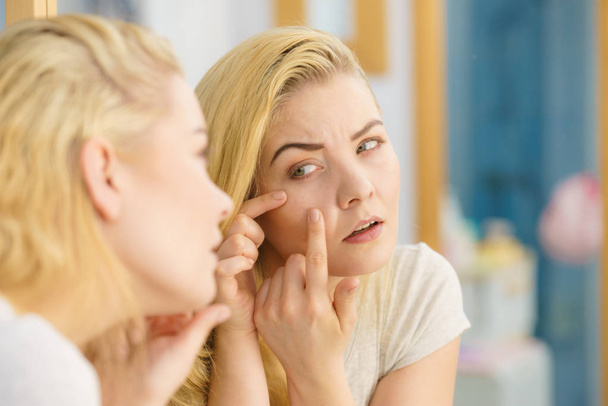Woman looking at her skin in mirror - Foto, afbeelding