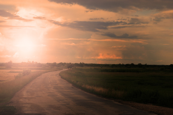 Camino de asfalto con nubes y rayos de sol al atardecer
 - Foto, Imagen