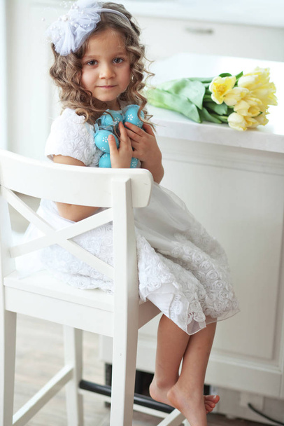 Beautiful little child wearing flower girl dress posing with the Easter eggs and bouquet of spring tulips - Foto, Imagem