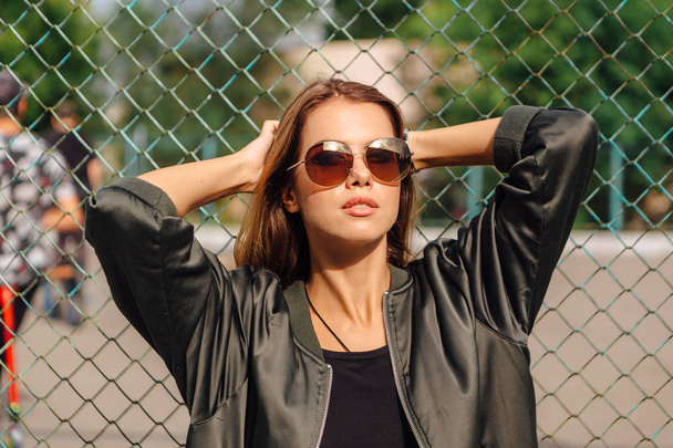 Fashion portrait of trendy young woman wearing sunglasses, and bomber jacket sitting next to rabitz in the city - Φωτογραφία, εικόνα