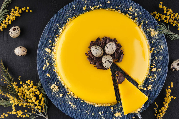 Πάσχα κέικ με κίτρινο καθρέφτης γλάσο, σοκολάτα, ανοιξιάτικα λουλούδια, τα αυγά ορτυκιού σε σκούρο φόντο πέτρα. Ευτυχή εορτασμό του Πάσχα. Το top view, επίπεδη lay - Φωτογραφία, εικόνα