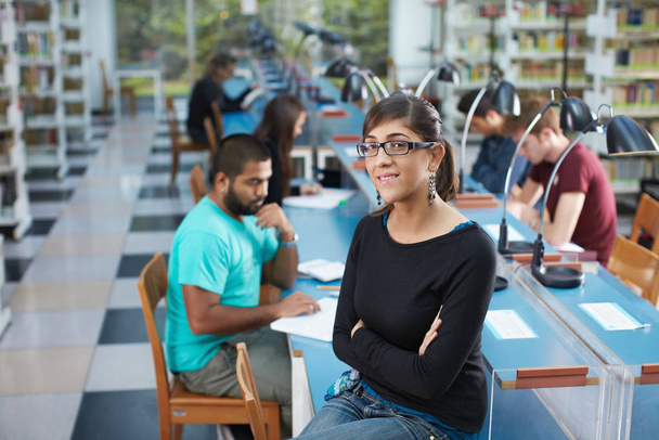 portrait of female college student sitting on table in library and looking at camera. Horizontal shape, waist up - Foto, imagen