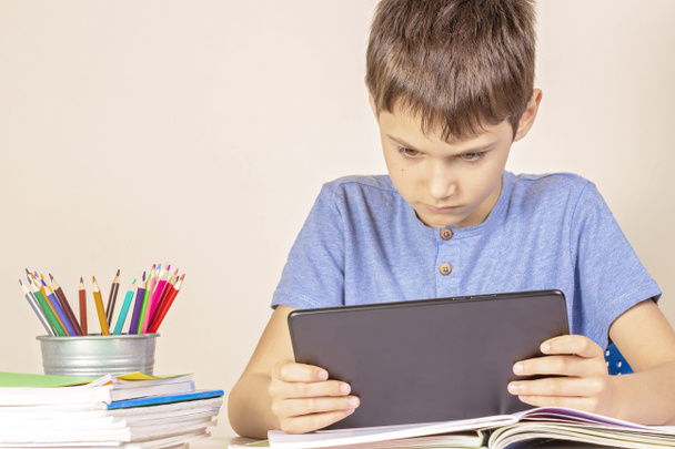 Дитина сидить за столом з книжковими блокнотами і використовує планшетний комп'ютер
 - Фото, зображення