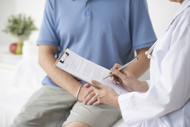 Doctor talking to patient and writing his complaints in medical history - Photo, Image