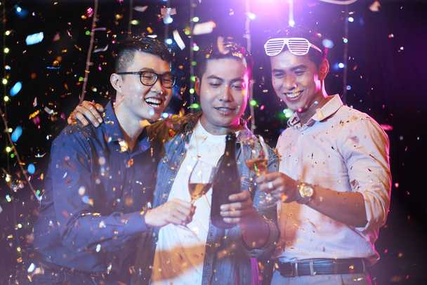 Joyful jóvenes asiáticos beber champán bajo la caída de confeti en la fiesta de noche
 - Foto, imagen