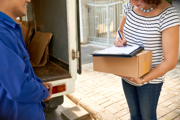 Woman receiving package from online store and signing document - Foto, Imagen