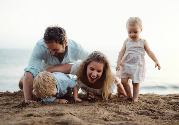 Young family with toddler children playing with sand on beach on summer holiday. - Photo, Image