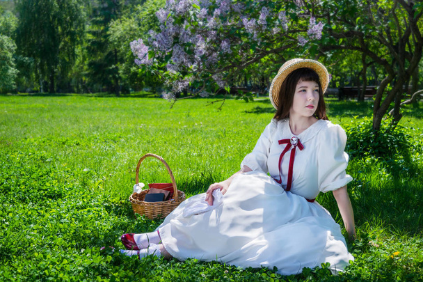 Girl in a white dress sitting under a tree lilacs. - Zdjęcie, obraz