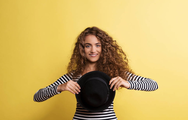 Portrait of a young woman with black hat in a studio on a yellow background. - Foto, Bild