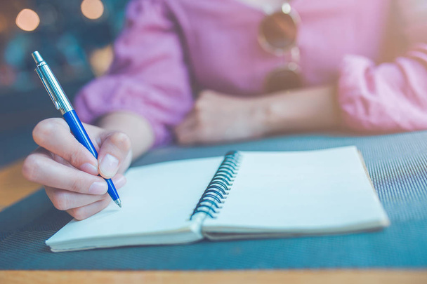 Γυναίκα χέρι γράφει σε ένα σημειωματάριο με στυλό. - Φωτογραφία, εικόνα