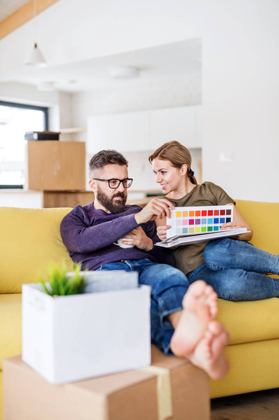 A young couple with color samples sitting on sofa, moving in new home. - Foto, imagen