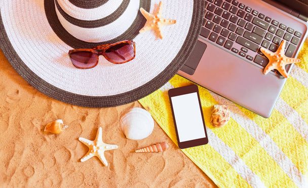Laptop and smart phone with beach items on sand beach.   - Zdjęcie, obraz