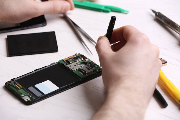 Technician fixing mobile phone at table, closeup. Device repair service - Photo, image