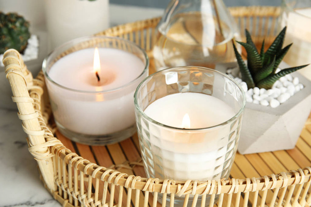 Wicker tray with burning candles and houseplant on table - Photo, image