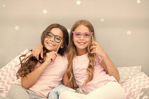 Birthday girl. Children posing with grimaces photo booth props. Pajamas party in bedroom. Friends cute and cheerful posing with eyeglasses accessories. Girls friends having fun pajamas party - 写真・画像