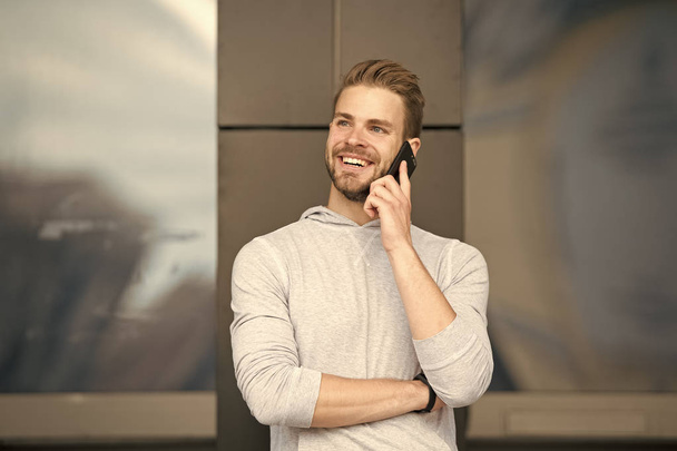 Man with beard call smartphone urban background. Guy happy smile use smartphone to communicate friends. Man use mobile phone call friend. Pleasant conversation concept. Glad to hear you - Foto, afbeelding