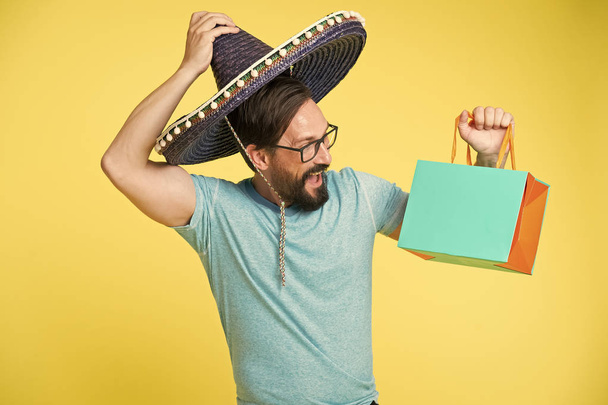 Man cheerful face sombrero hat holds shopping bag yellow background. Guy with beard festive in sombrero. Man festive mood holds shopping bag. Seasonal sale and discount. Holiday and gift concept - Fotoğraf, Görsel