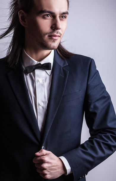 elegancki młody przystojny długowłosy mężczyzna w stroju. Studio moda piękny portret. - Zdjęcie, obraz