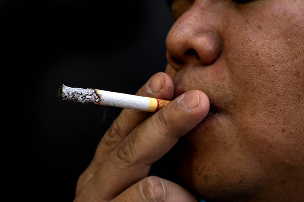 Мужчина курит сигарету, изображение сигареты в руке с дымом
 - Фото, изображение