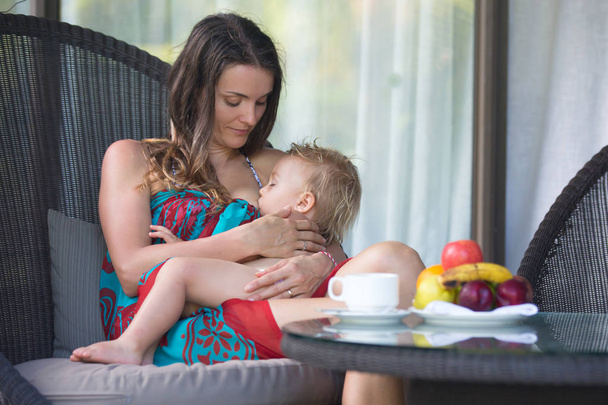 Portrait of beautiful young woman breastfeeding toddler boy on b - Фото, зображення