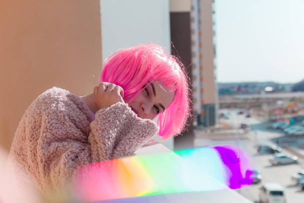 young beautiful hipster woman in street style fashion pink fur coat standing on a balcony - Photo, Image