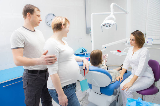 A female dentist communicates with a child and her family in a dental clinic. The mother of the girl is pregnant - Photo, Image