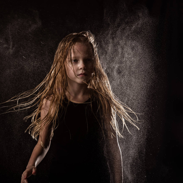 young girl with live emotions dancing under water drops. child splashing water on a dark background - Fotografie, Obrázek