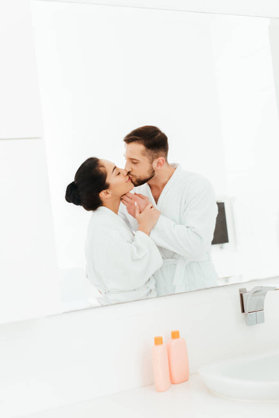Szczęśliwa kobieta całuje z chłopakiem stojąc w pobliżu lustro w łazience - Zdjęcie, obraz