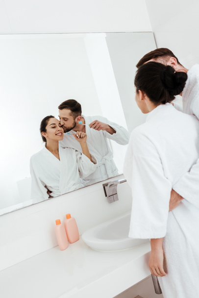 Brodaty człowiek całuje policzek wesoły kobieta patrząc na lustro w łazience  - Zdjęcie, obraz