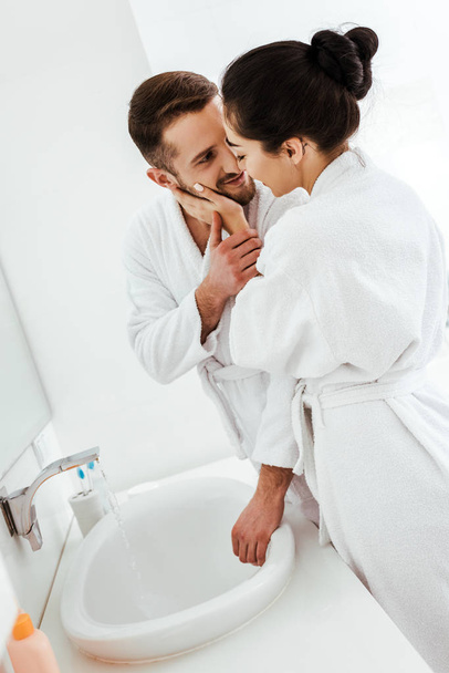 brunette girl touching face of handsome man smiling in bathrobe  - Photo, Image